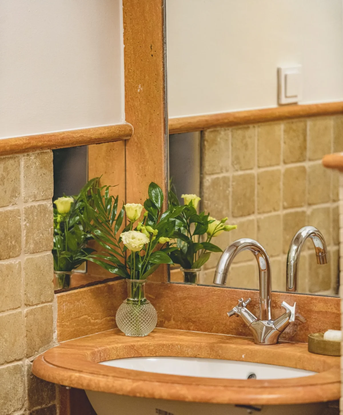 Close-up of chrome tap, marble washbasin and fresh yellow roses in the Deluxe Double bathroom