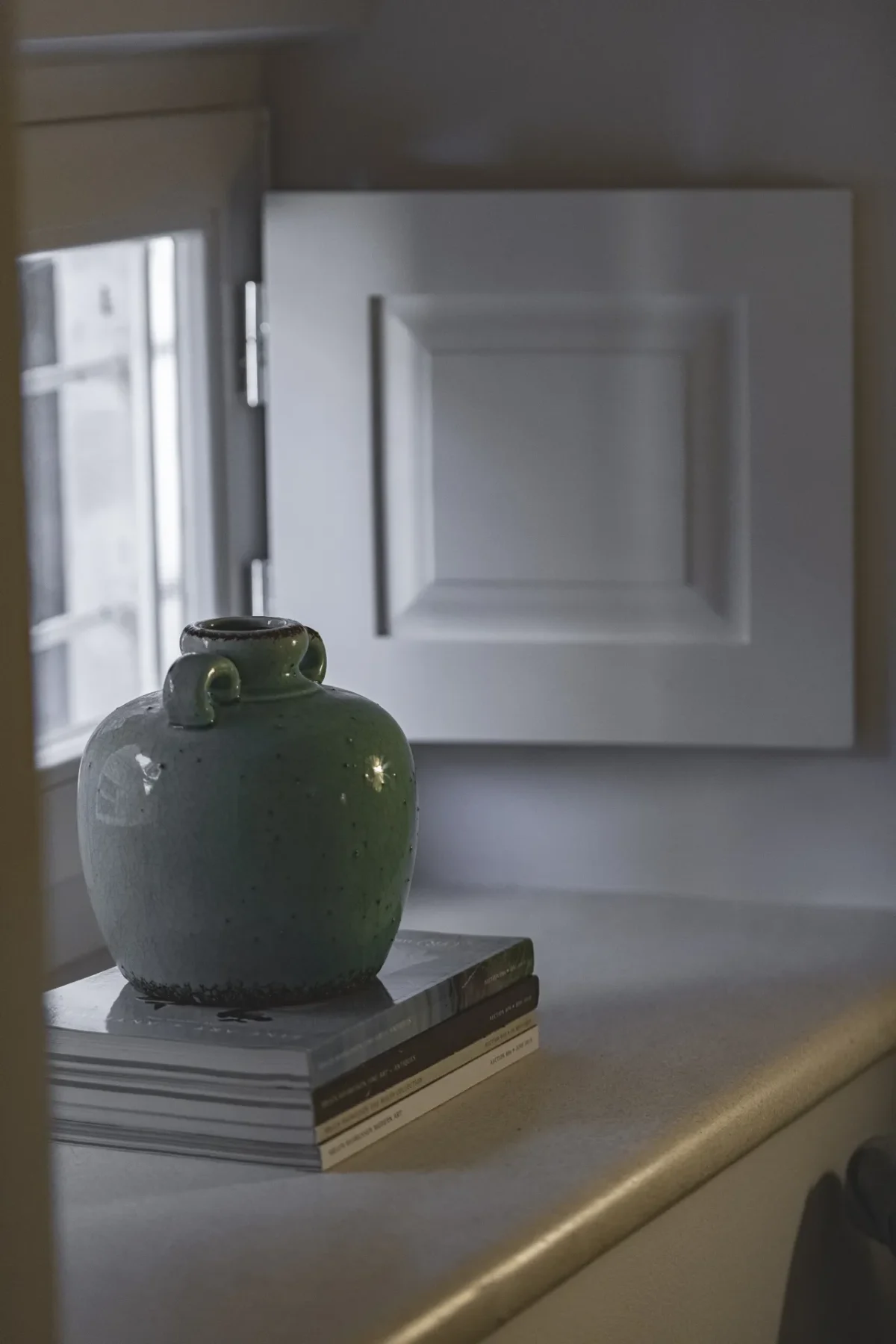 Green ceramic vase on stacked books beside a white-shuttered window at Dominus Little Palace