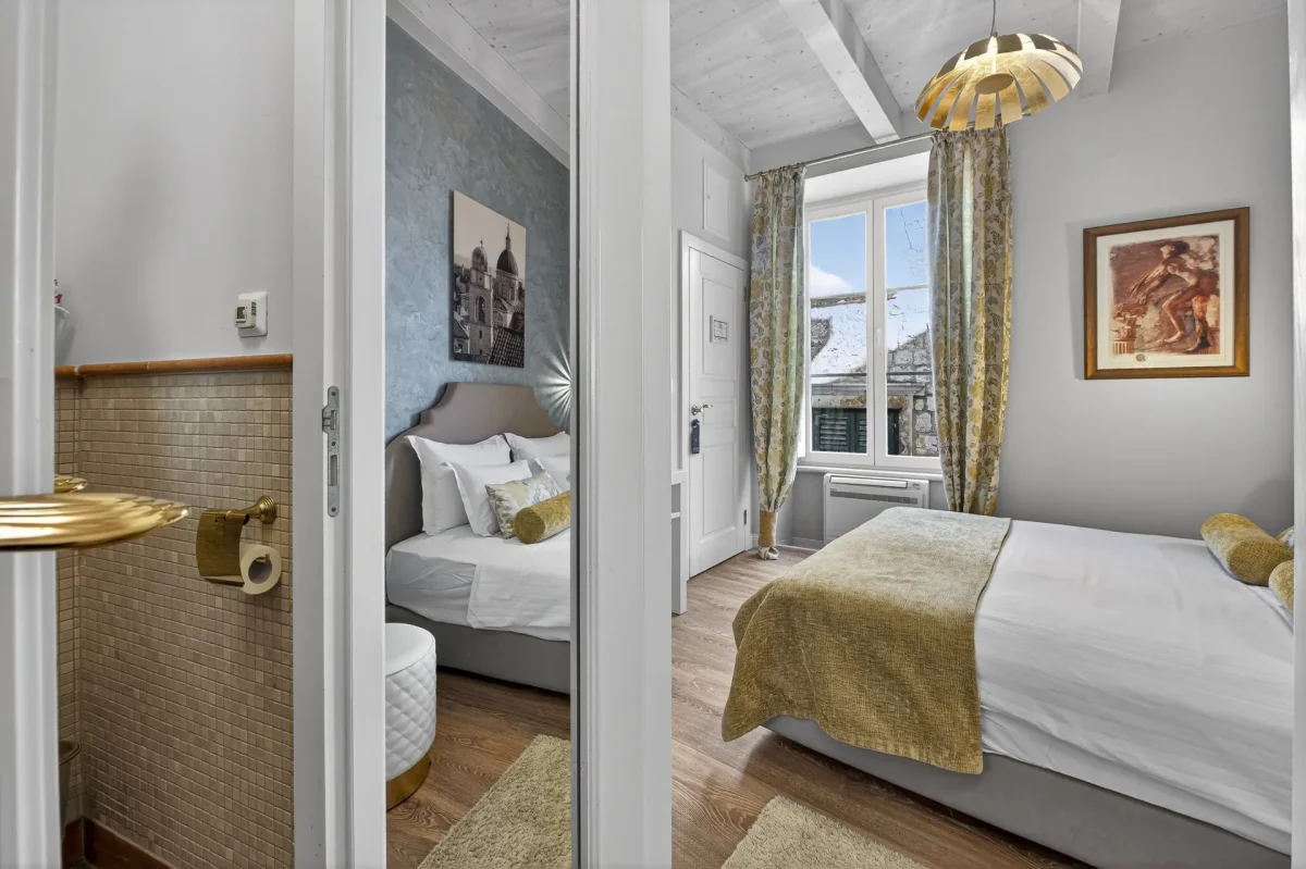 View from the en-suite bathroom into the Deluxe Double Room with curtained window and Dubrovnik Cathedral print