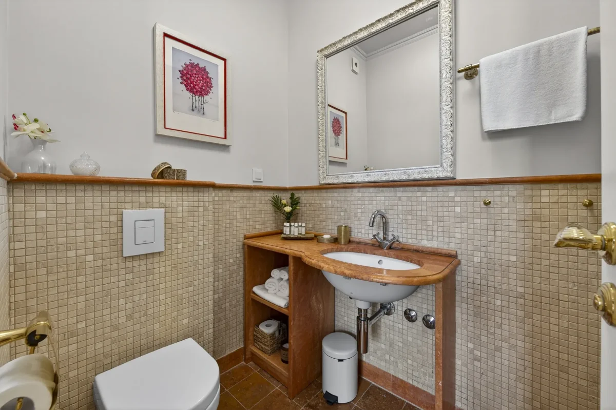 En-suite bathroom of the Deluxe Double Room with travertine mosaic tiles, wooden vanity and ornate silver mirror