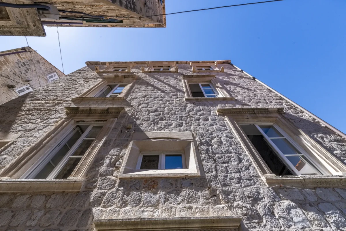 Looking up at the restored stone facade and carved window frames of Dominus Little Palace in Dubrovnik