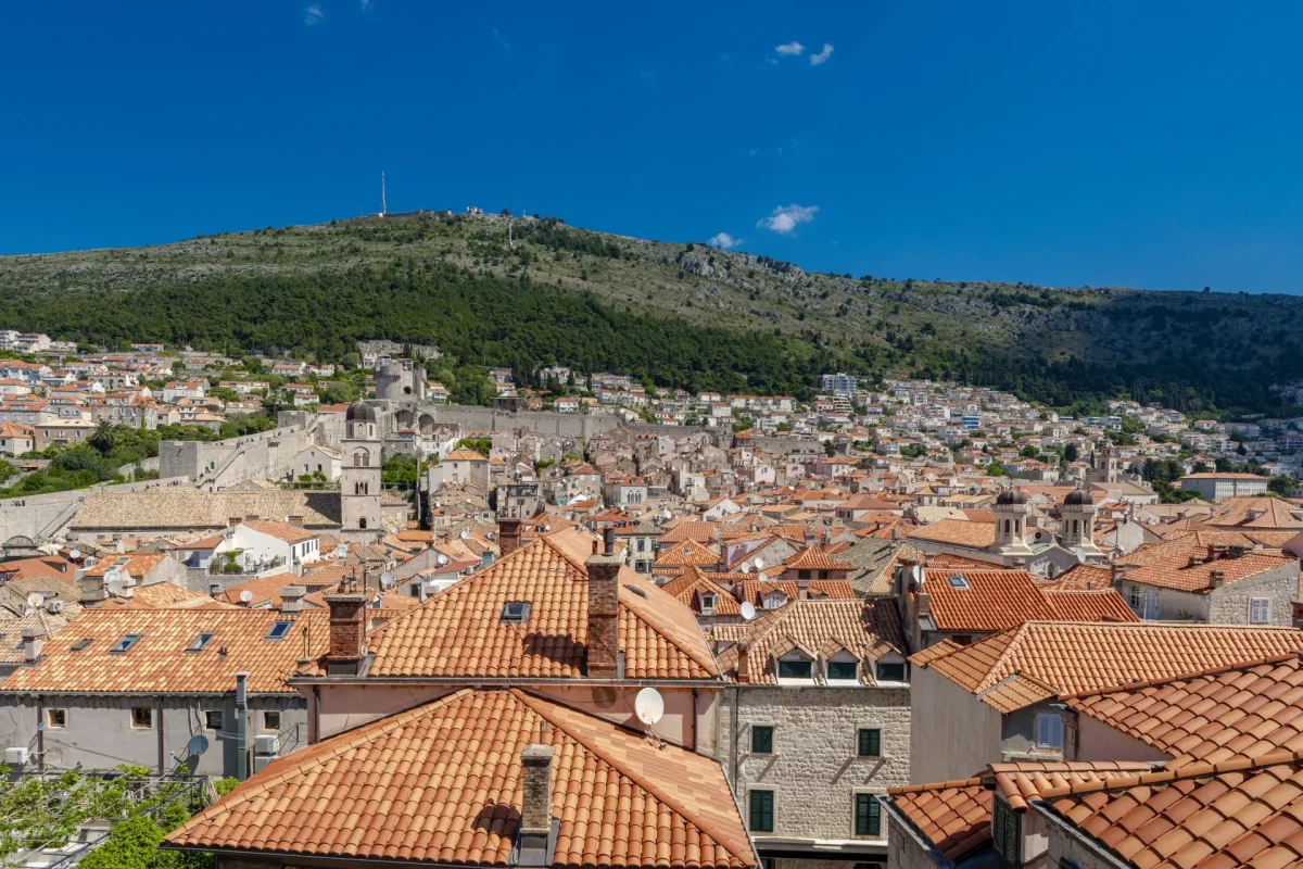 Terracotta rooftops of Dubrovnik Old Town with the city walls, Minčeta Tower and Mount Srđ under a blue sky
