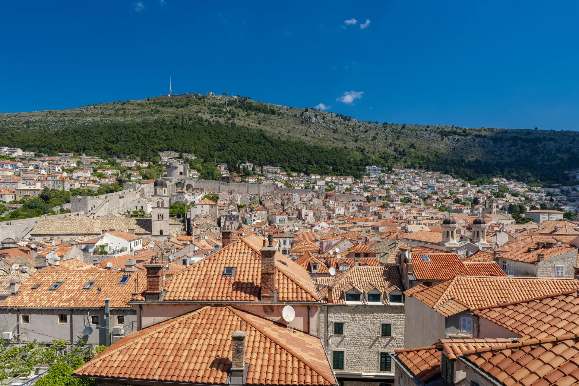 Terracotta rooftops of Dubrovnik Old Town with the city walls, Minčeta Tower and Mount Srđ under a blue sky