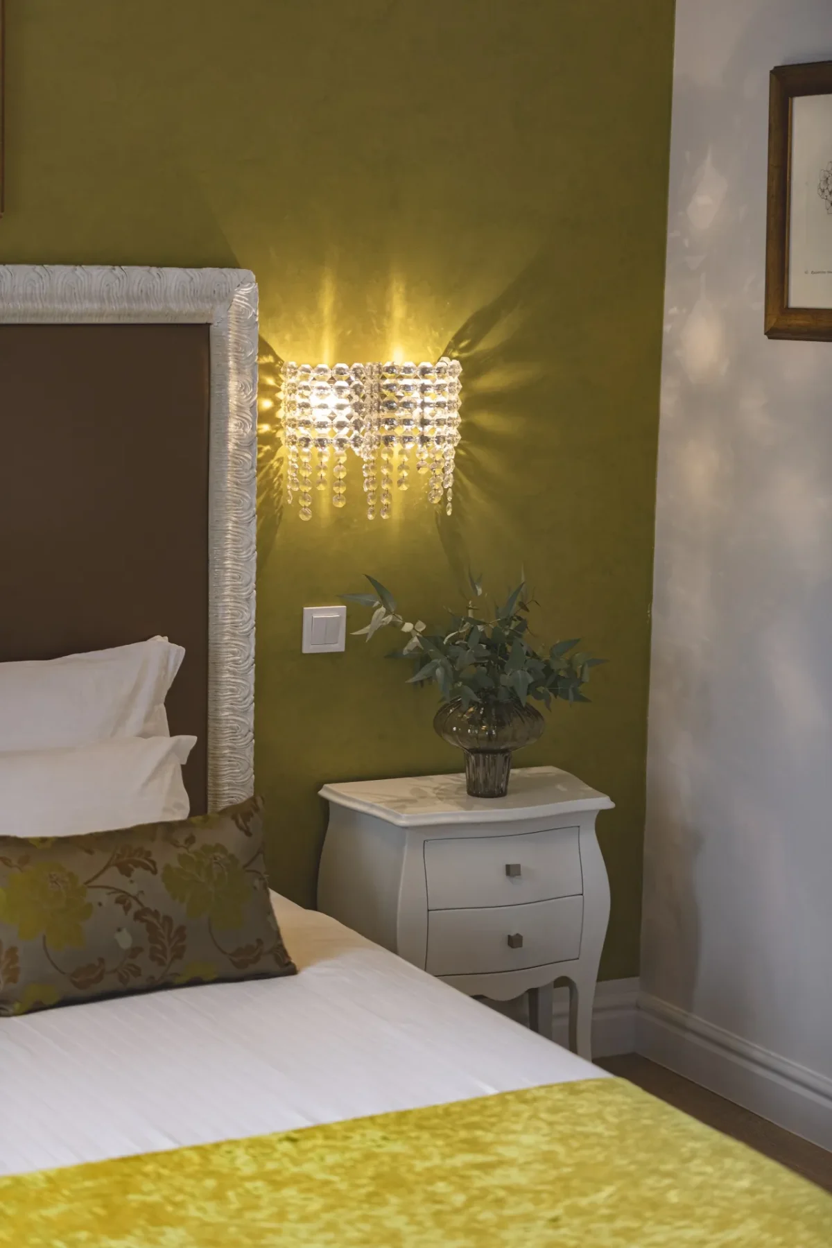 Softly lit bedside corner with crystal sconce and olive-green wall in the Executive Suite at Dominus Little Palace
