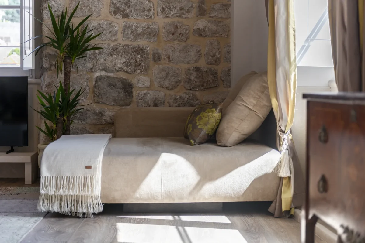 Sunlit daybed with cream throw against an exposed stone wall in the Executive Suite, Dubrovnik