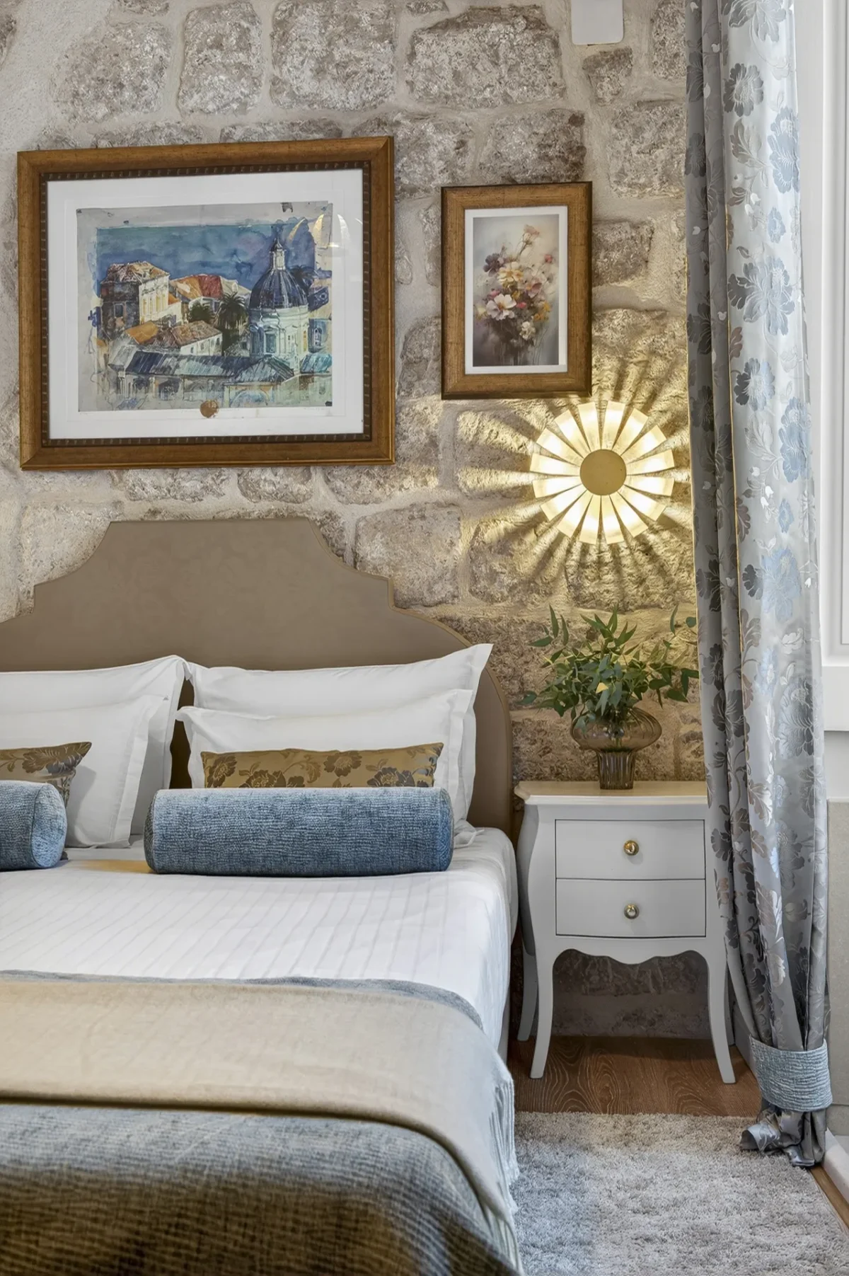 Framed Dubrovnik artworks and sunburst wall lamp above the bed in the Premium Double Room