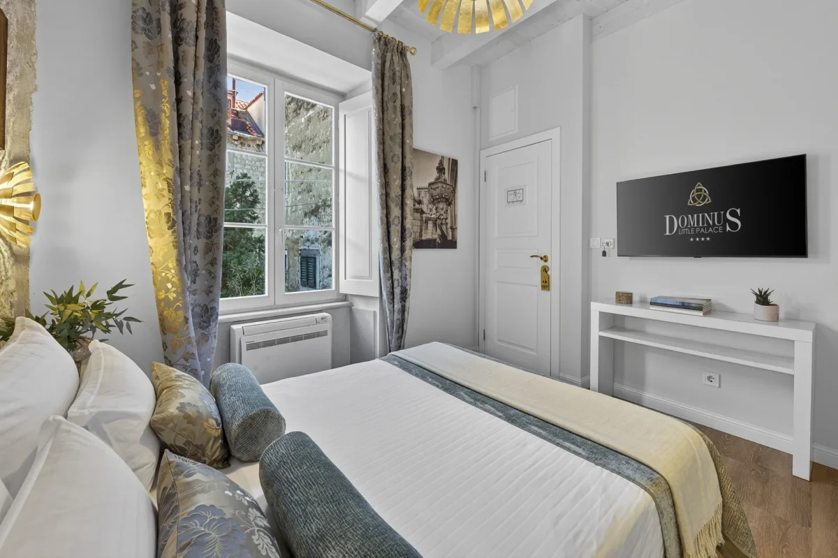 Premium Double Room with wall-mounted TV showing the Dominus Little Palace logo, desk and tall window